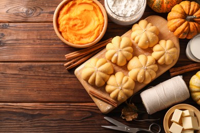 Photo of Raw pumpkin shaped buns and ingredients on wooden table, flat lay. Space for text