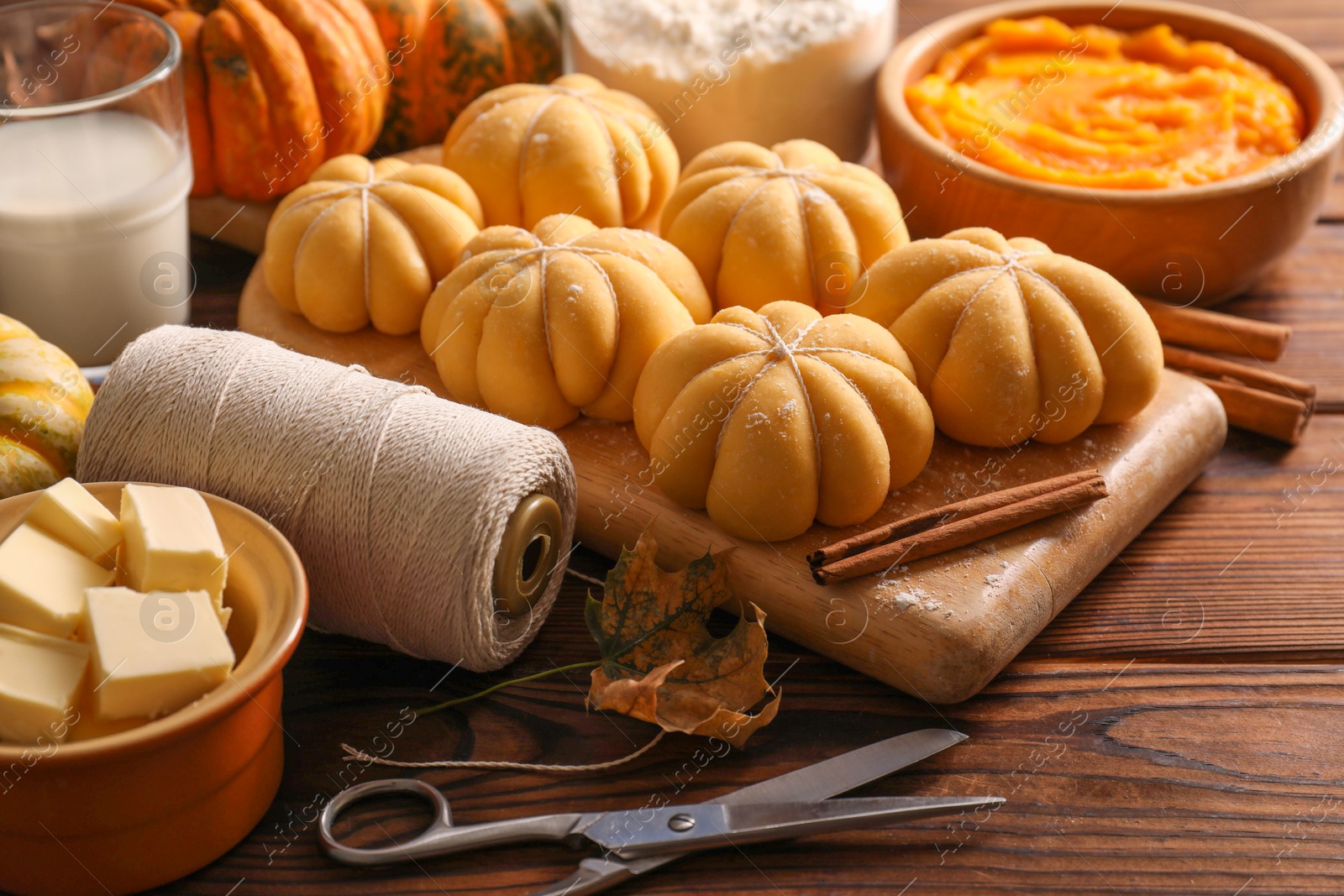 Photo of Raw pumpkin shaped buns and ingredients on wooden table