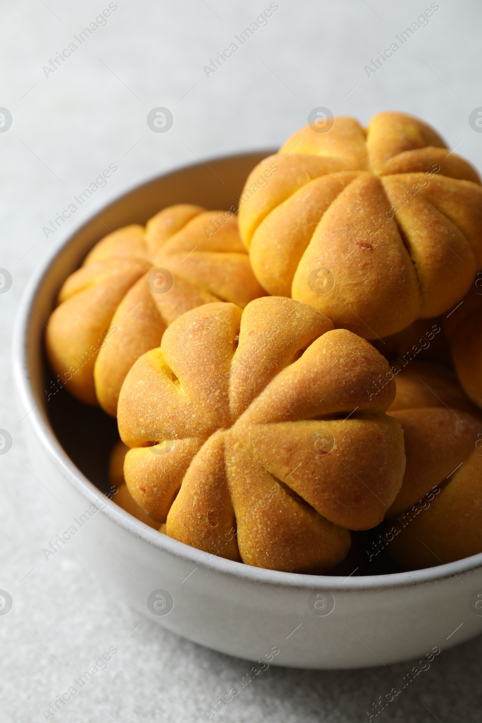 Photo of Tasty pumpkin shaped buns in bowl on grey table, closeup