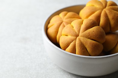 Photo of Tasty pumpkin shaped buns in bowl on grey table, closeup. Space for text