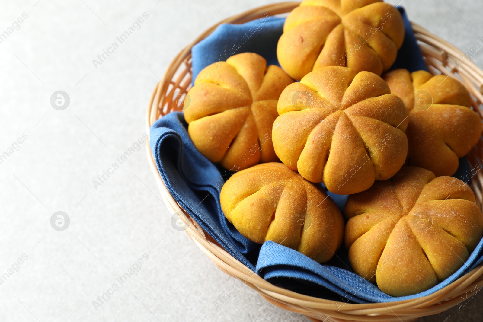 Photo of Wicker basket with tasty pumpkin shaped buns on light table, closeup. Space for text