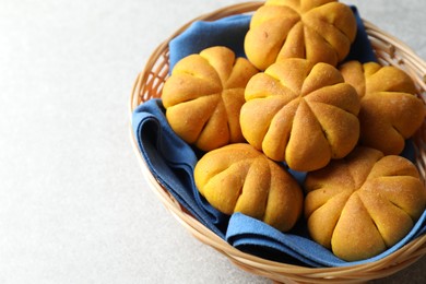 Photo of Wicker basket with tasty pumpkin shaped buns on light table, closeup. Space for text