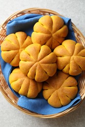 Photo of Wicker basket with tasty pumpkin shaped buns on light table, top view