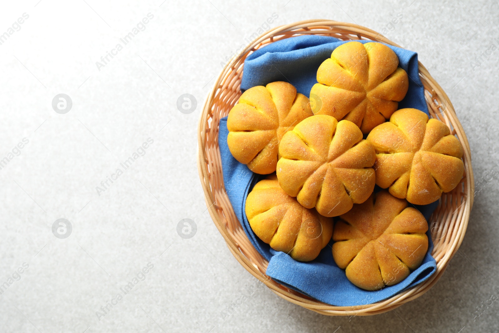 Photo of Wicker basket with tasty pumpkin shaped buns on light table, top view. Space for text