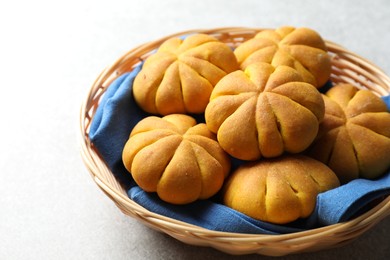 Photo of Wicker basket with tasty pumpkin shaped buns on light table, closeup