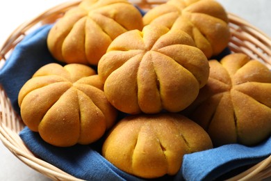 Photo of Wicker basket with tasty pumpkin shaped buns on table, closeup