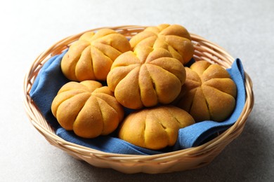 Photo of Wicker basket with tasty pumpkin shaped buns on light table, closeup