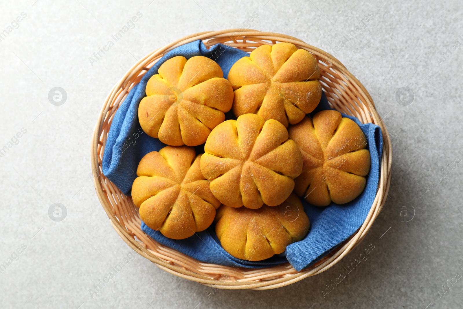 Photo of Wicker basket with tasty pumpkin shaped buns on grey table, top view