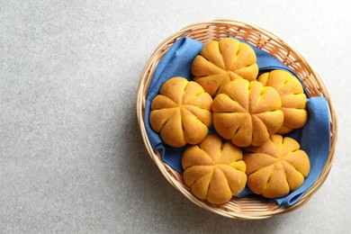 Photo of Wicker basket with tasty pumpkin shaped buns on light table, top view. Space for text