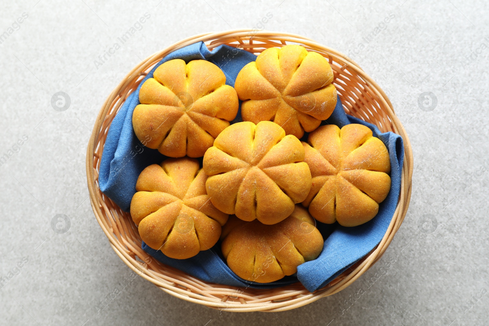 Photo of Wicker basket with tasty pumpkin shaped buns on grey table, top view