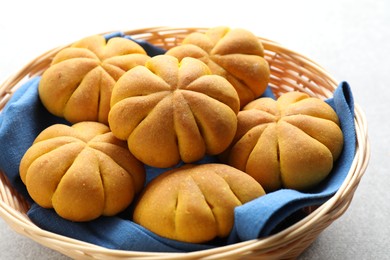 Photo of Wicker basket with tasty pumpkin shaped buns on light table, closeup