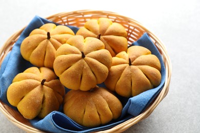 Photo of Wicker basket with tasty pumpkin shaped buns on light table, closeup