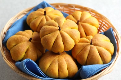 Photo of Wicker basket with tasty pumpkin shaped buns on light table, closeup