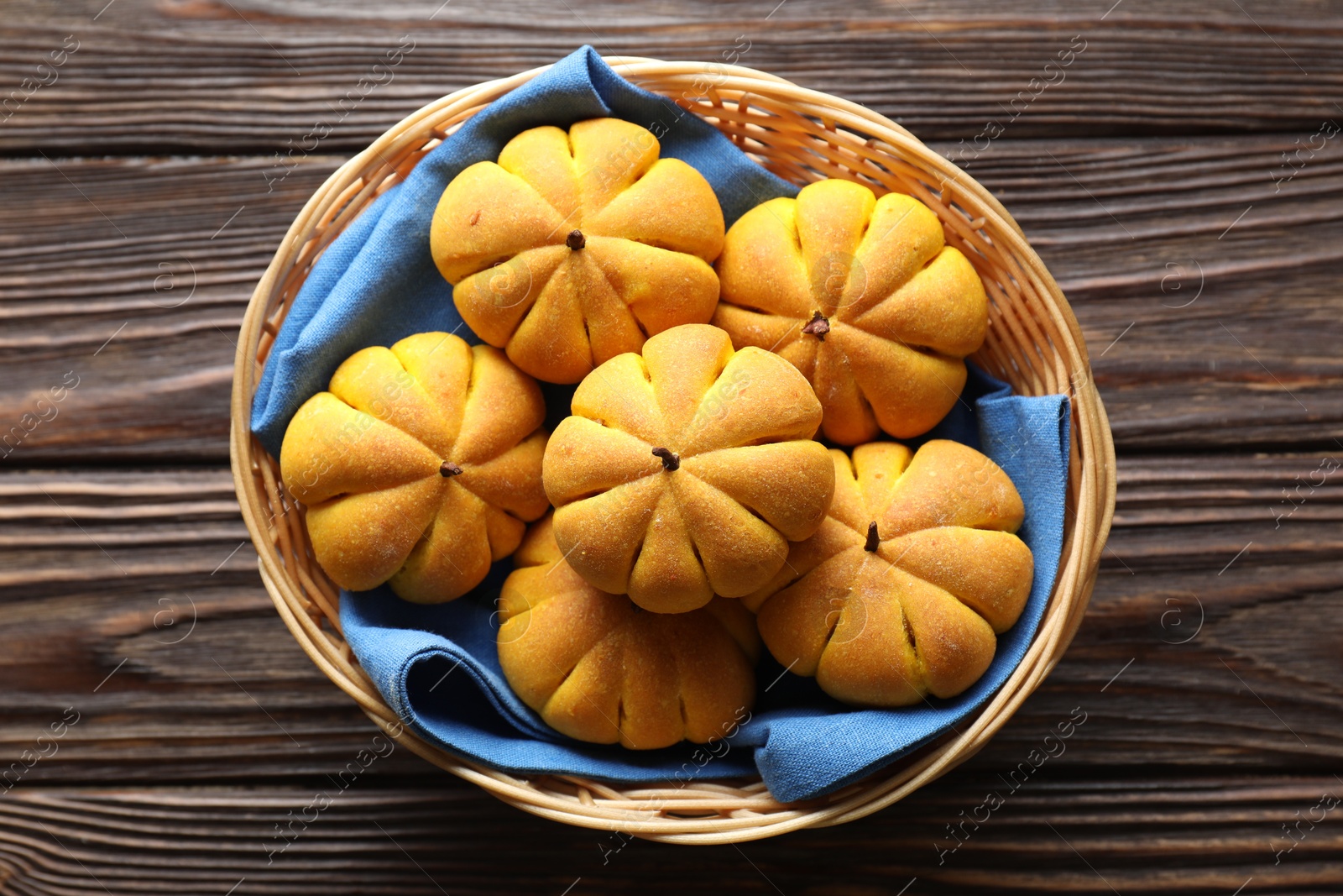 Photo of Wicker basket with tasty pumpkin shaped buns on wooden table, top view