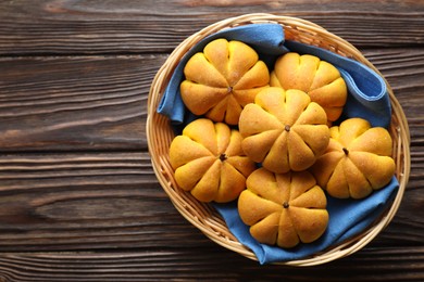 Photo of Wicker basket with tasty pumpkin shaped buns on wooden table, top view. Space for text