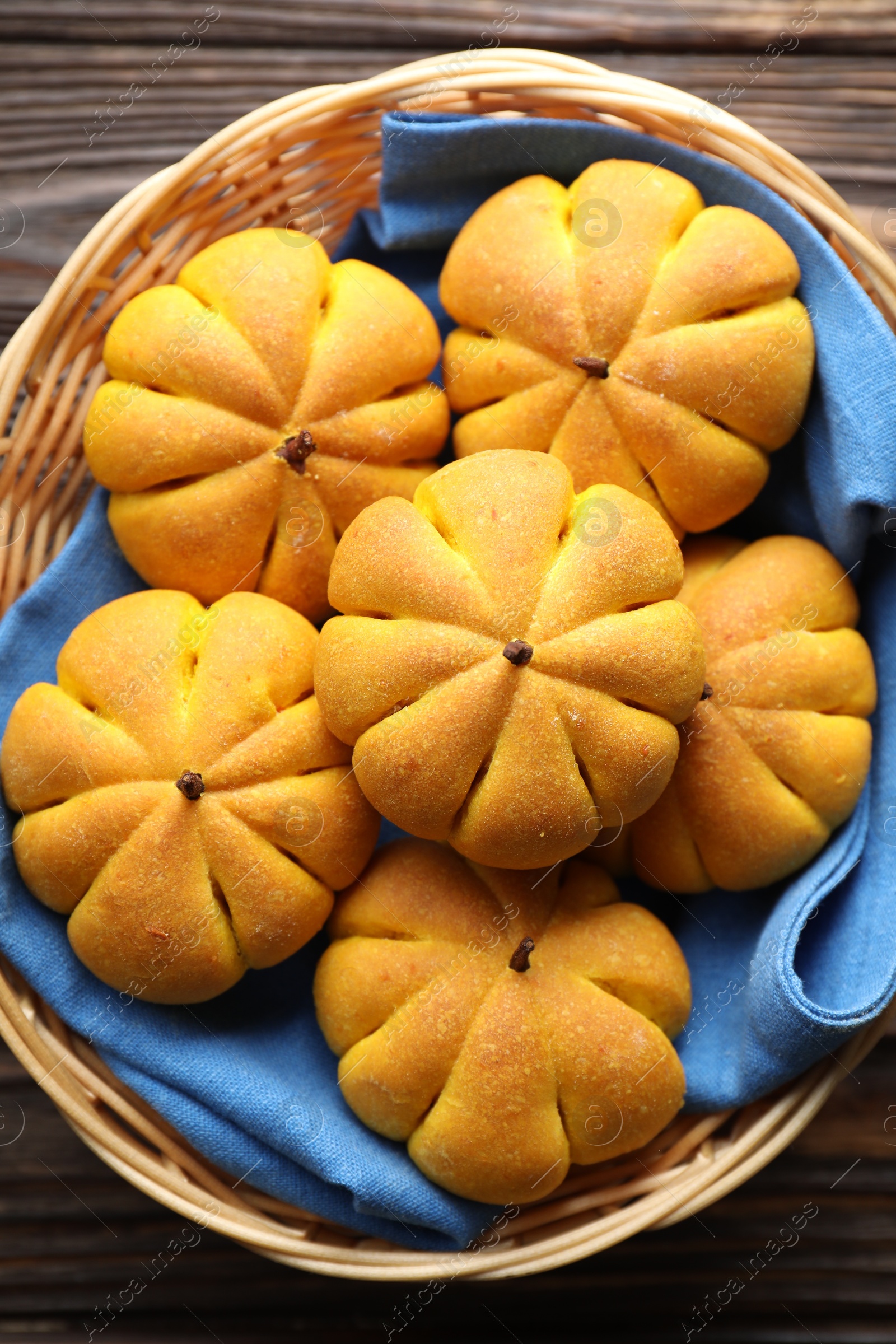 Photo of Wicker basket with tasty pumpkin shaped buns on wooden table, top view