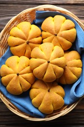 Photo of Wicker basket with tasty pumpkin shaped buns on wooden table, top view