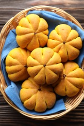 Photo of Wicker basket with tasty pumpkin shaped buns on wooden table, top view