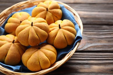 Photo of Wicker basket with tasty pumpkin shaped buns on wooden table, closeup