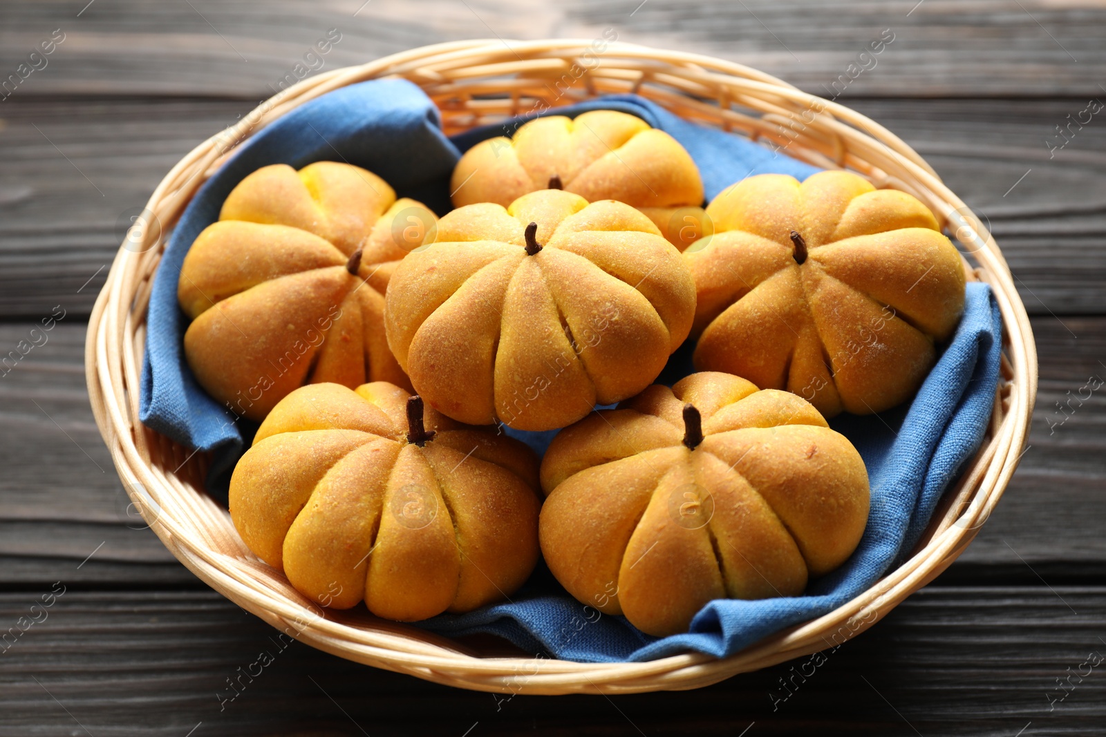 Photo of Wicker basket with tasty pumpkin shaped buns on wooden table, closeup