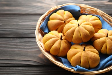 Photo of Wicker basket with tasty pumpkin shaped buns on wooden table, closeup