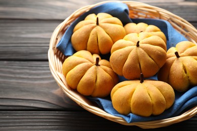 Photo of Wicker basket with tasty pumpkin shaped buns on wooden table, closeup