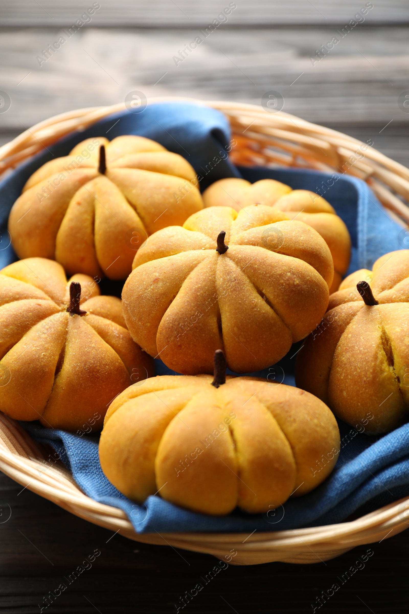 Photo of Wicker basket with tasty pumpkin shaped buns on wooden table, closeup