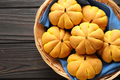 Photo of Wicker basket with tasty pumpkin shaped buns on wooden table, top view. Space for text