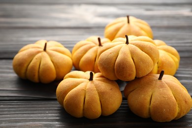 Photo of Pile of tasty pumpkin shaped buns on wooden table, closeup