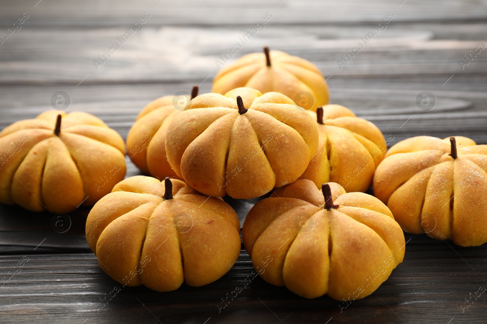 Photo of Pile of tasty pumpkin shaped buns on wooden table, closeup