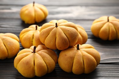 Photo of Pile of tasty pumpkin shaped buns on wooden table, closeup