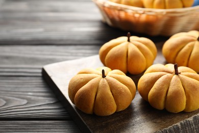 Photo of Tasty pumpkin shaped buns on wooden table, closeup. Space for text