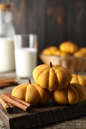 Photo of Tasty pumpkin shaped buns and cinnamon sticks on wooden table, closeup