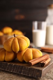 Photo of Tasty pumpkin shaped buns and cinnamon sticks on wooden table, closeup