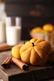 Photo of Tasty pumpkin shaped buns and cinnamon sticks on wooden board, closeup