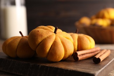 Photo of Tasty pumpkin shaped buns and cinnamon sticks on wooden board, closeup