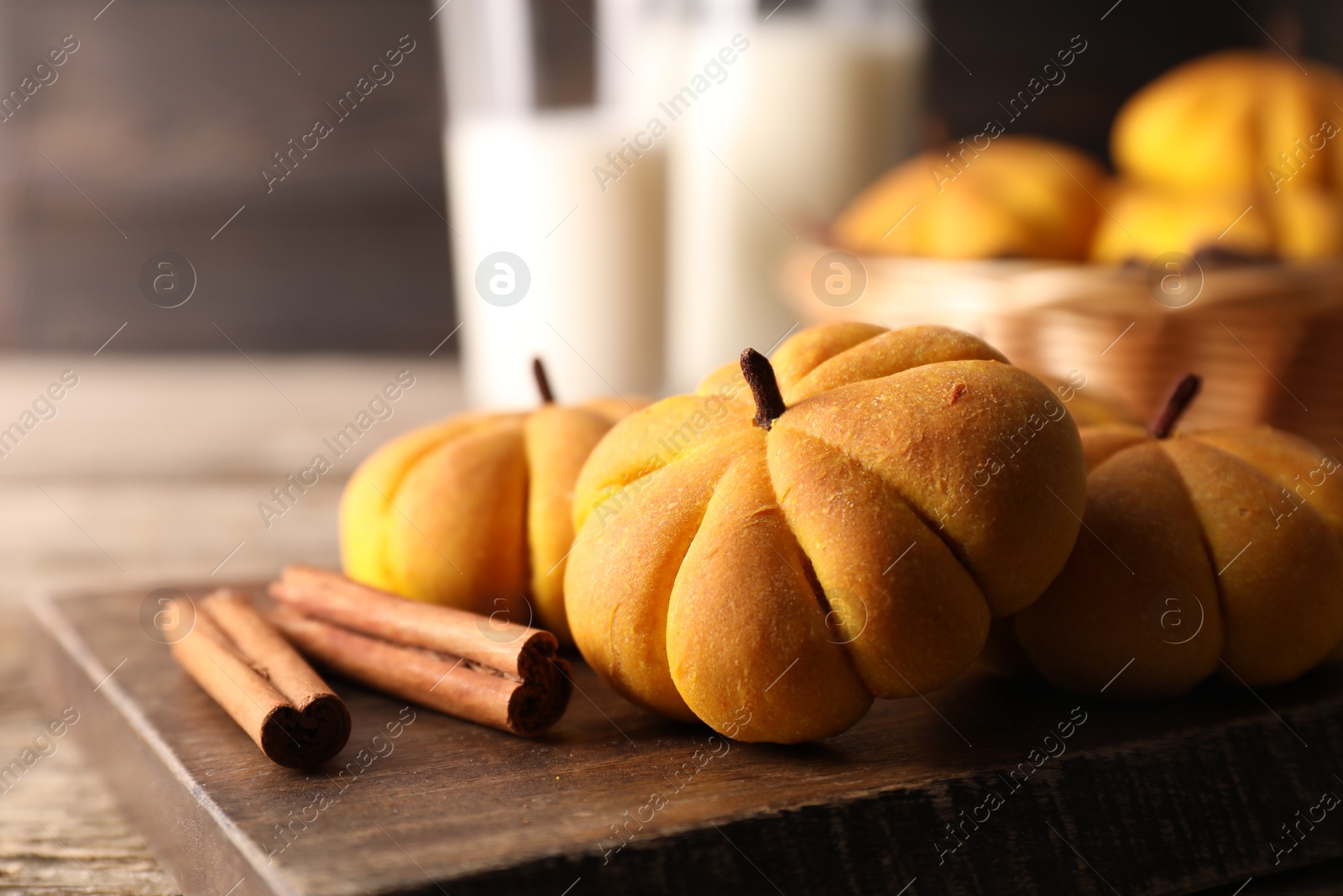 Photo of Tasty pumpkin shaped buns and cinnamon sticks on wooden table, closeup