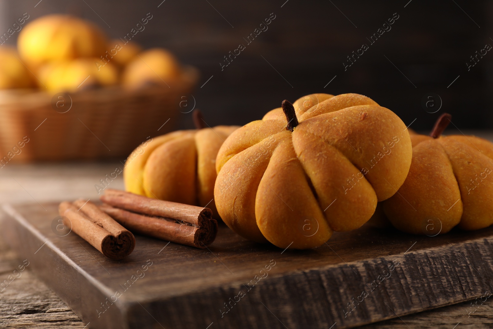 Photo of Tasty pumpkin shaped buns and cinnamon sticks on wooden table, closeup