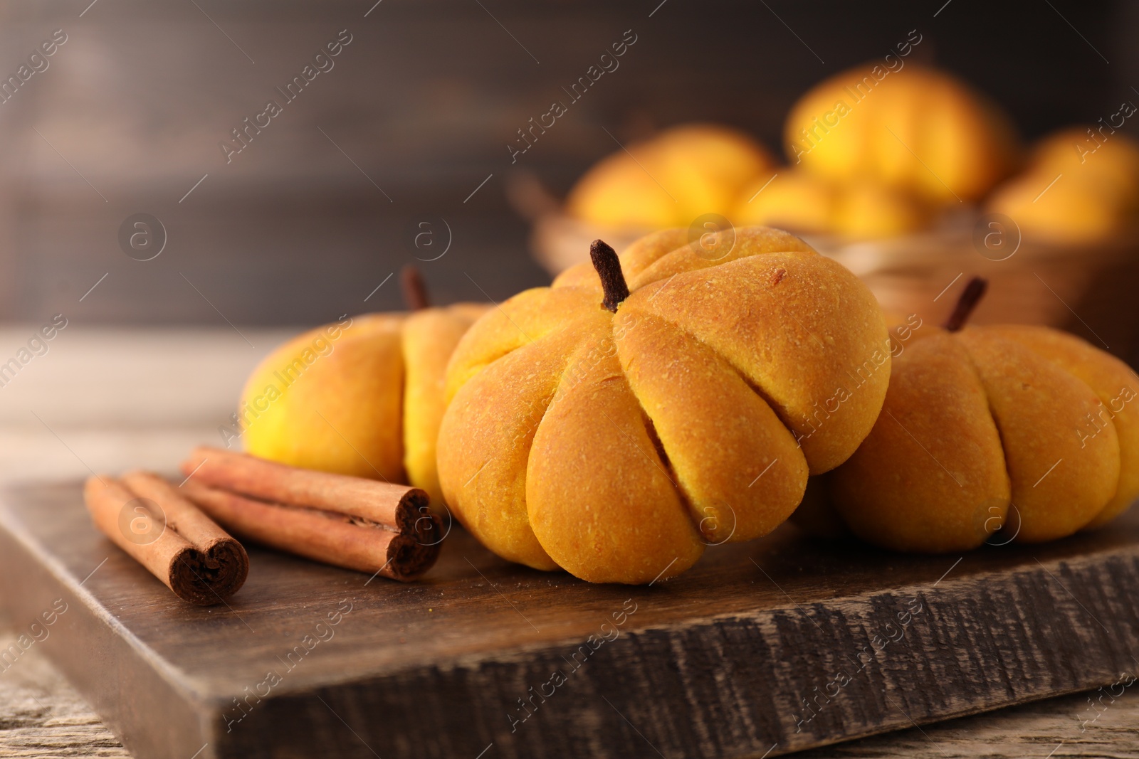 Photo of Tasty pumpkin shaped buns and cinnamon sticks on wooden table, closeup