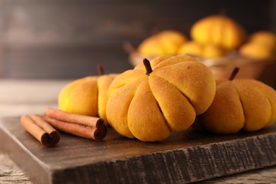 Photo of Tasty pumpkin shaped buns and cinnamon sticks on wooden table, closeup