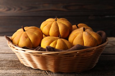 Photo of Wicker basket with tasty pumpkin shaped buns on wooden table, closeup