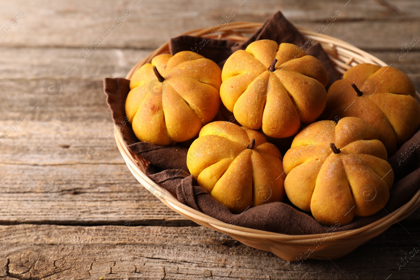 Photo of Wicker basket with tasty pumpkin shaped buns on wooden table, closeup. Space for text