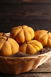 Photo of Wicker basket with tasty pumpkin shaped buns on wooden table, closeup