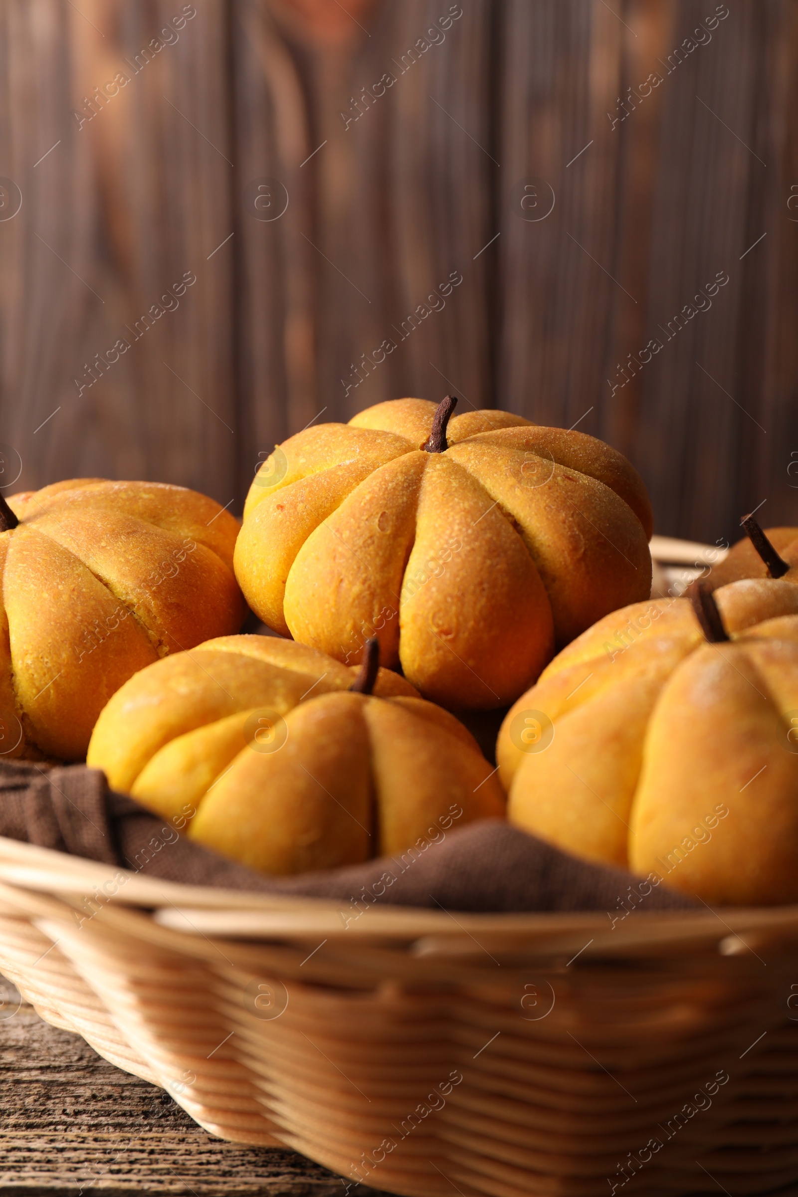 Photo of Wicker basket with tasty pumpkin shaped buns on wooden table, closeup