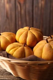 Photo of Wicker basket with tasty pumpkin shaped buns on wooden table, closeup