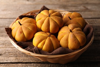 Photo of Wicker basket with tasty pumpkin shaped buns on wooden table, closeup