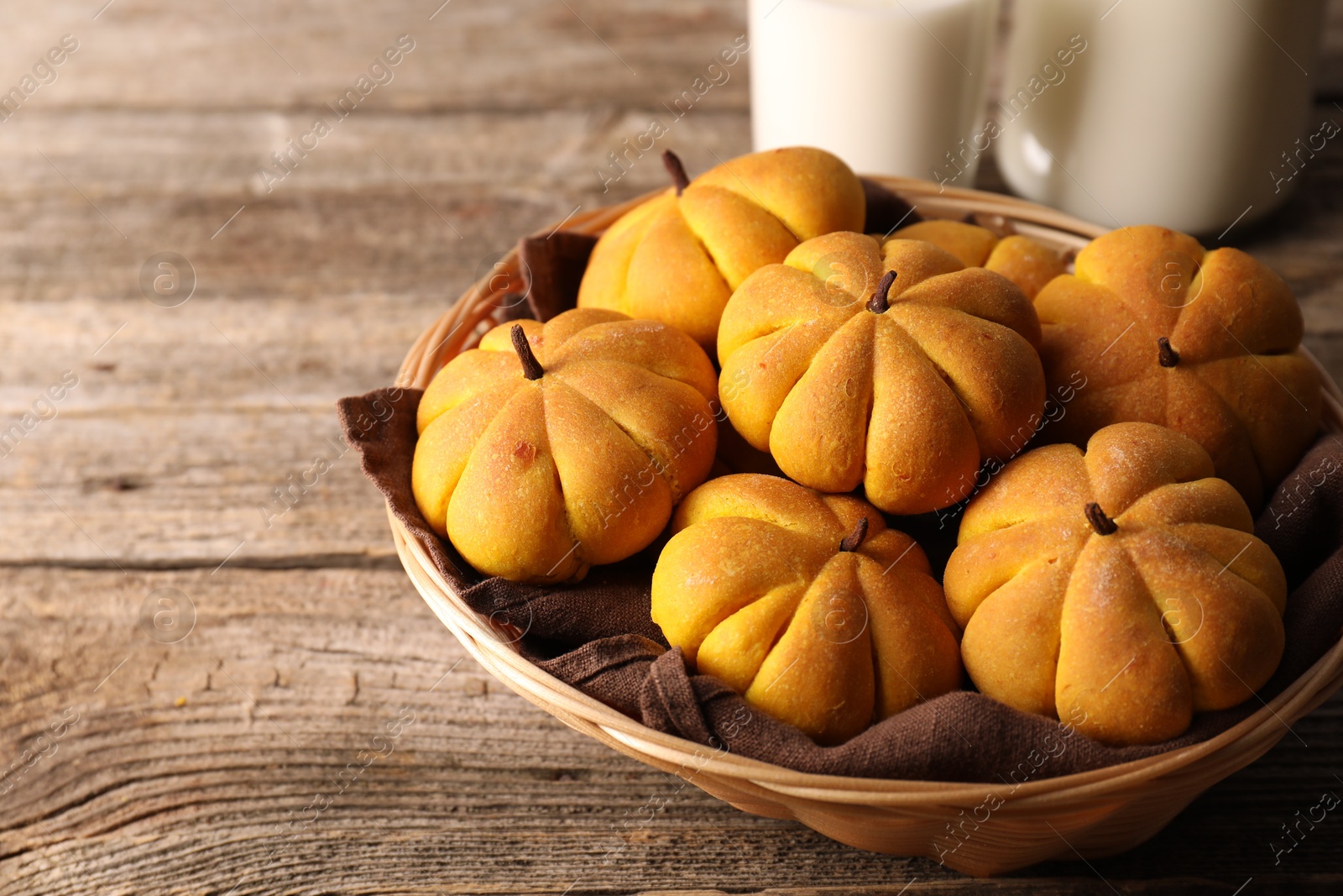 Photo of Wicker basket with tasty pumpkin shaped buns on wooden table, closeup. Space for text