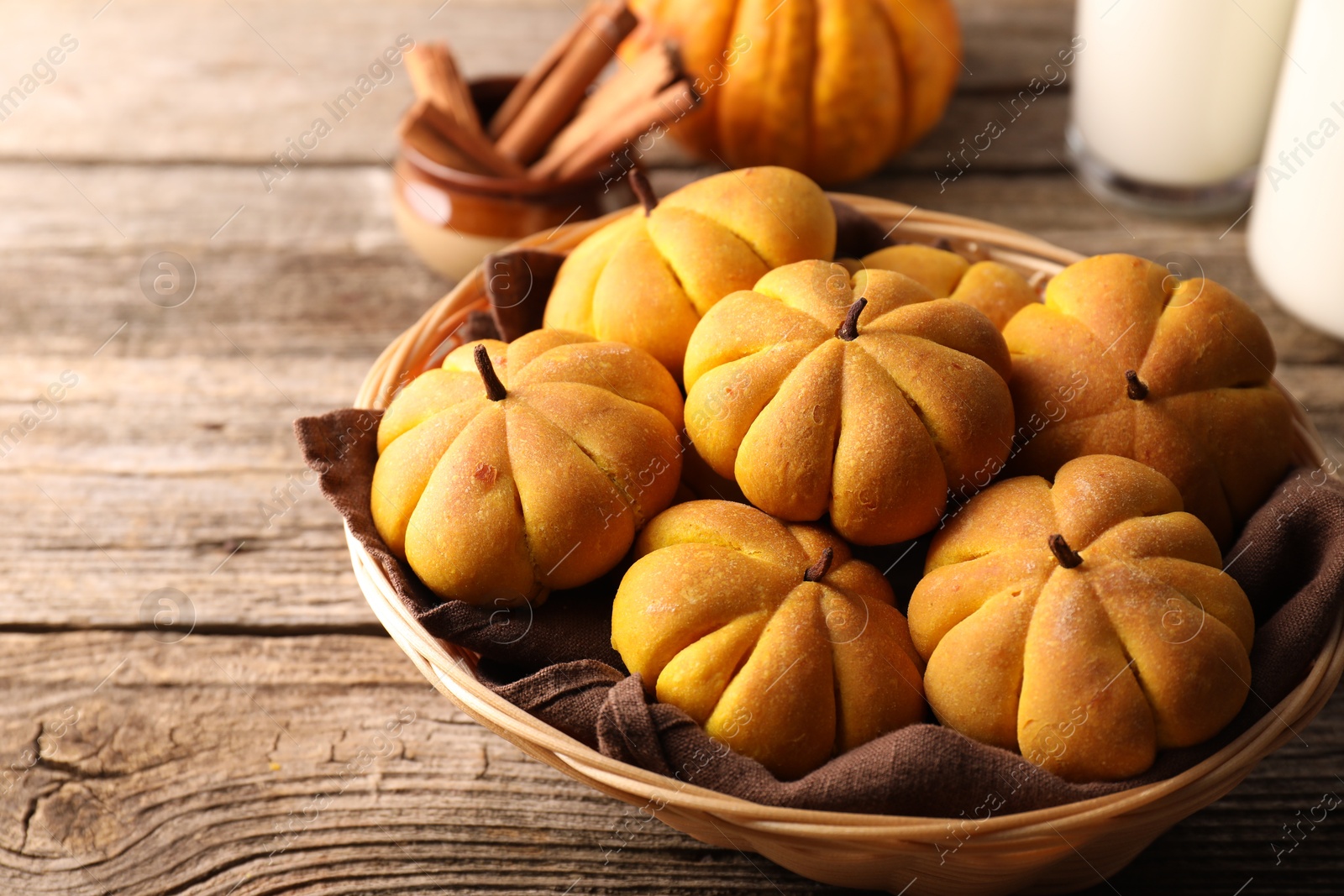 Photo of Wicker basket with tasty pumpkin shaped buns on wooden table, closeup