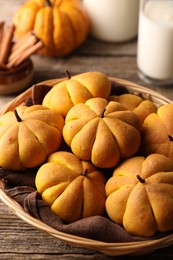 Photo of Wicker basket with tasty pumpkin shaped buns on wooden table, closeup