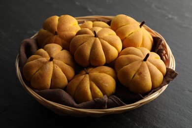 Photo of Wicker basket with tasty pumpkin shaped buns on dark textured table, closeup